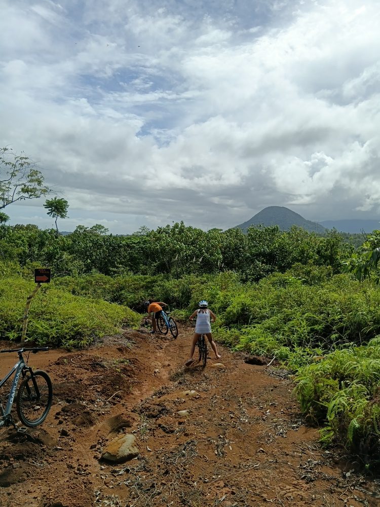 Riders seen from behind on the red-dirt farm trail, with Susong Dalaga ahead