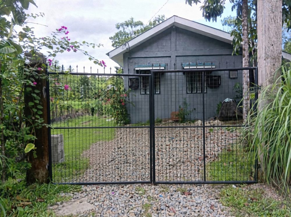 The grey house behind a black metal gate and gravel drive