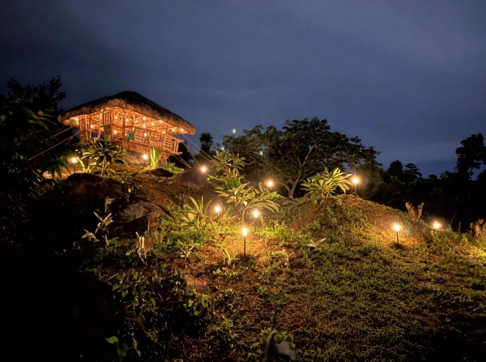 The house on the hill at night, with a lit path and string lights