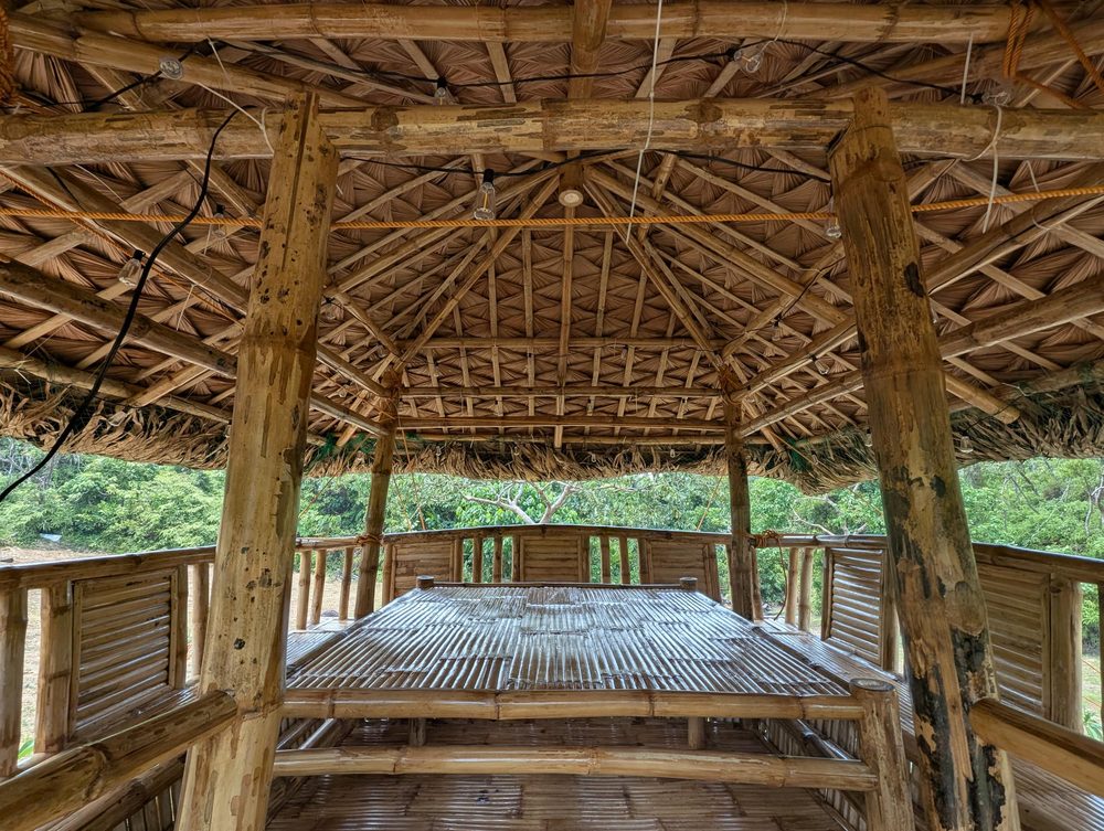 Inside the thatched nipa palapa, with a wooden table and benches